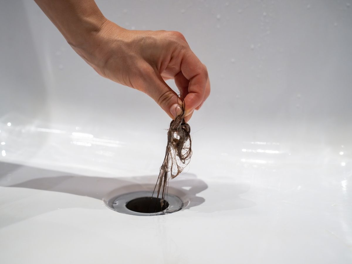 Hand removing hair from bathroom drain