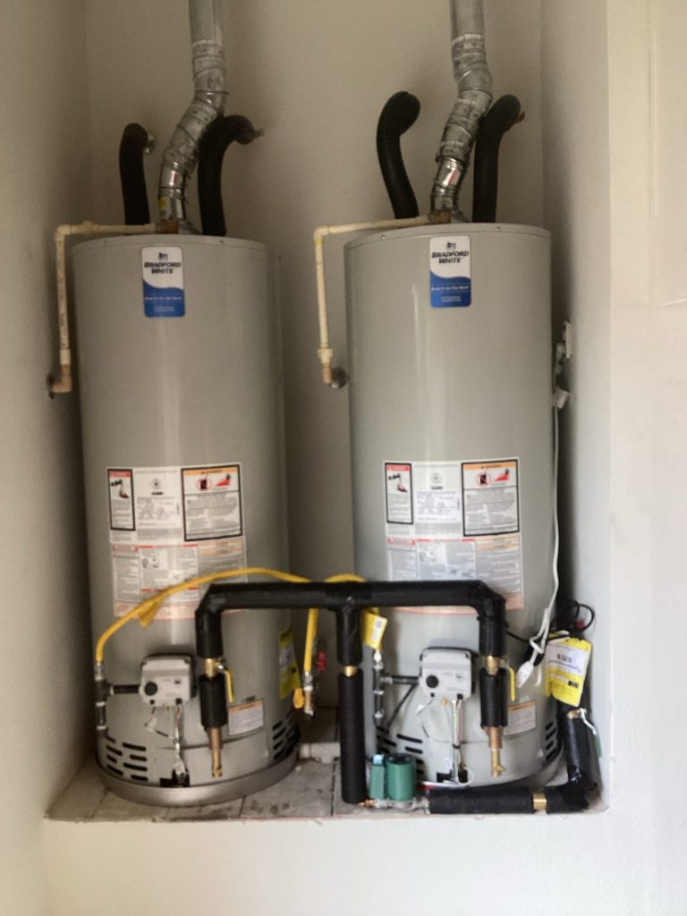 Two installed hot water heaters with pipes and labels.